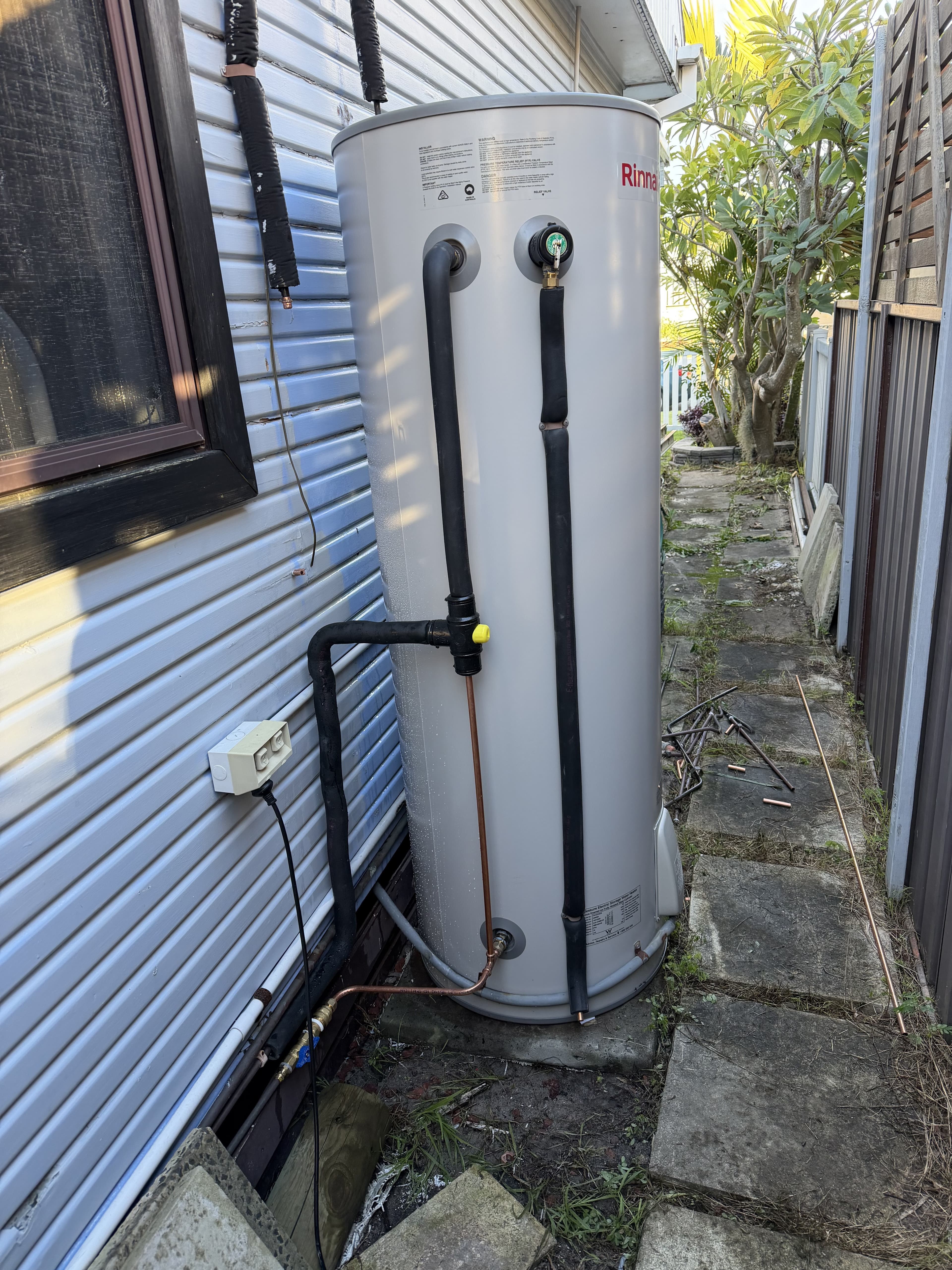 Newly installed hot water storage tank plumbed in against a house wall